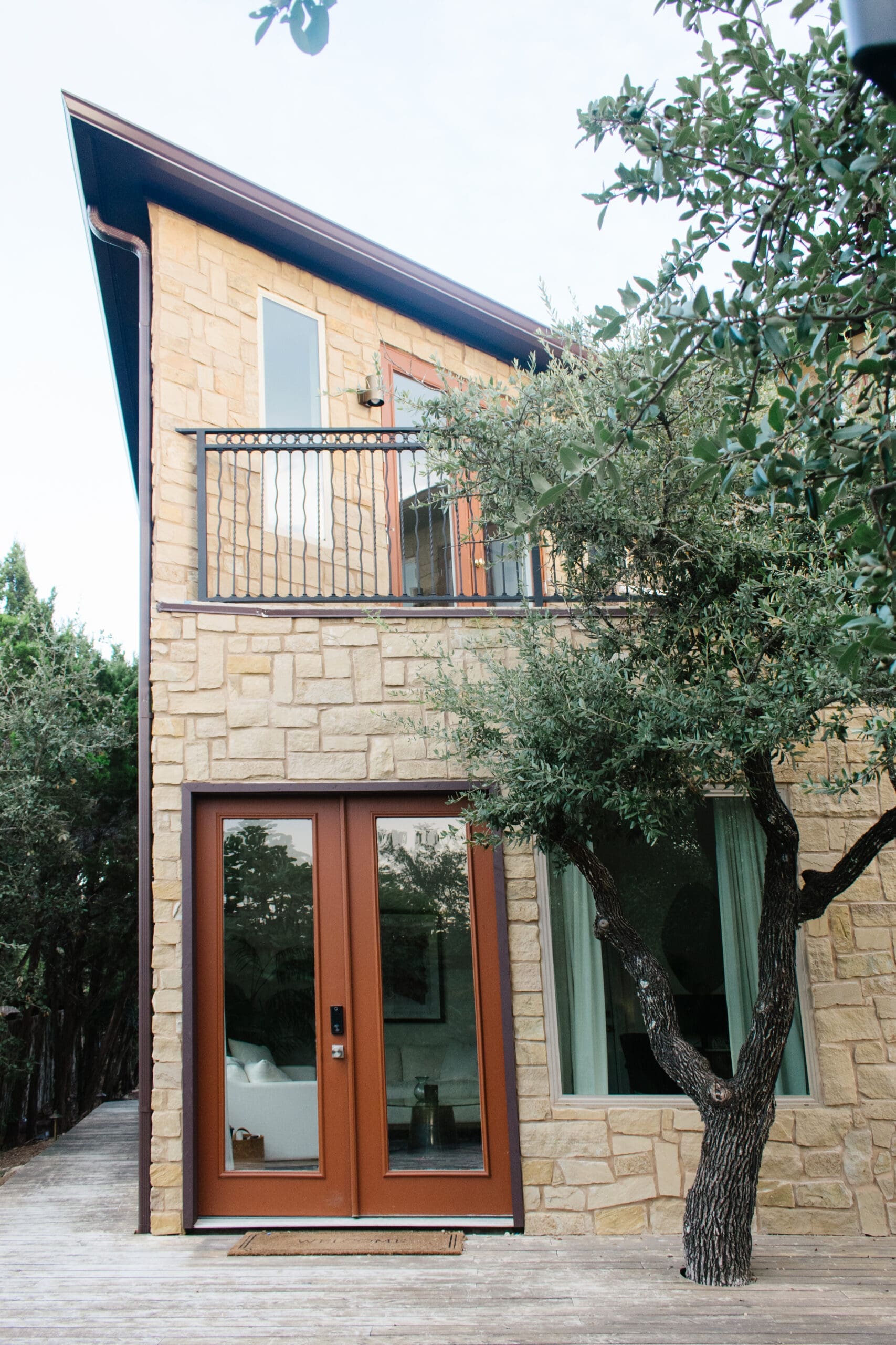 Stone home exterior with a balcony and mature oak trees