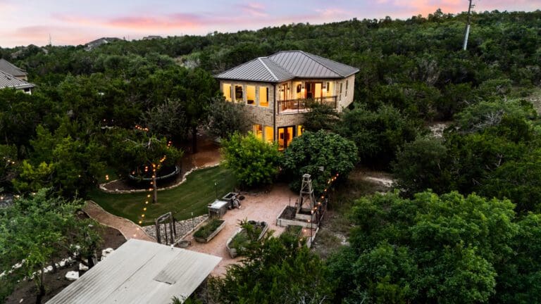 Two-story casita guest house lit at dusk among oak trees in Dripping Springs